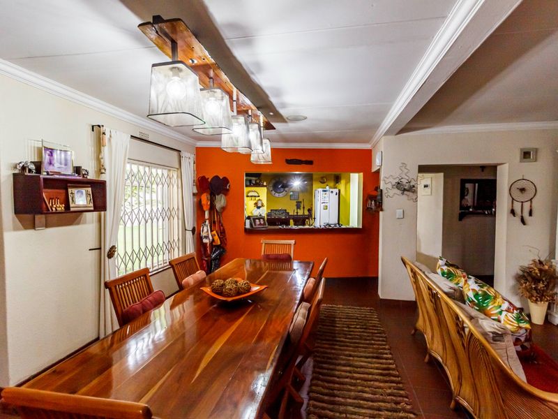 Open-plan dining and living area featuring a pass-through window to the kitchen, tiled flooring, and decorative pendant lighting.