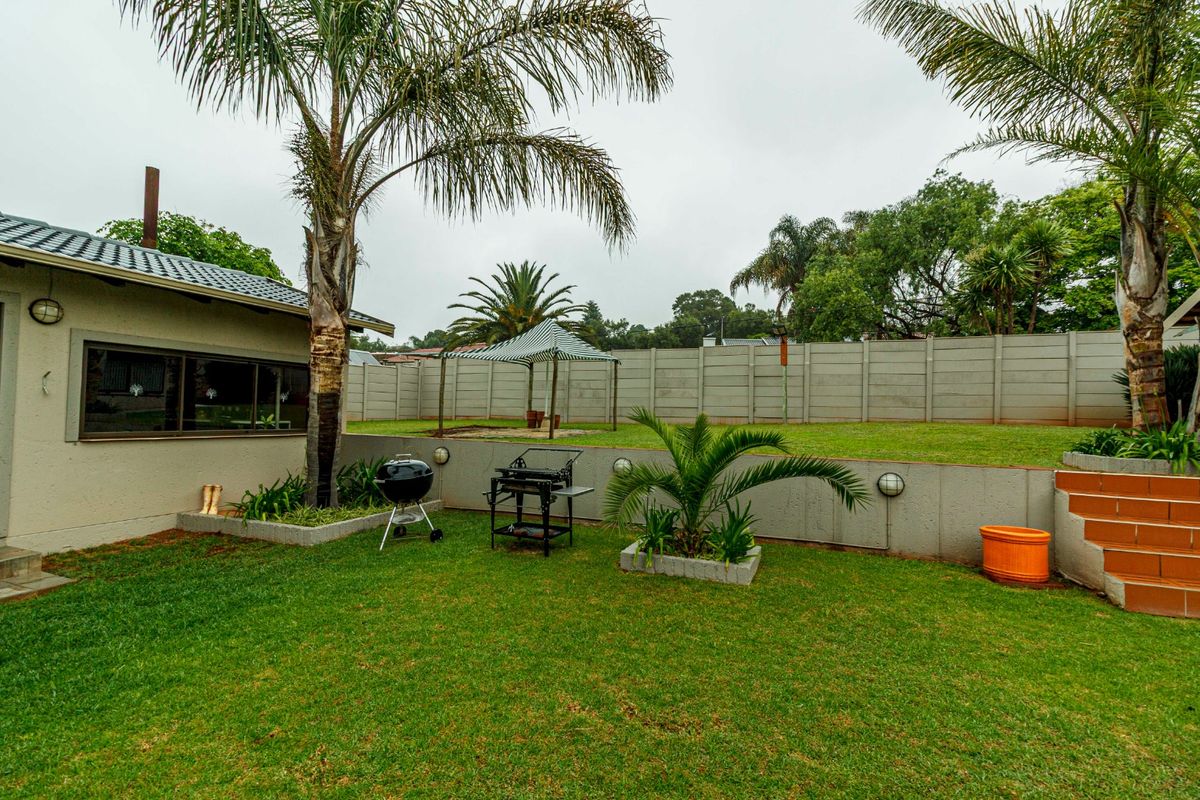 A spacious rear garden featuring a lawn, retaining wall, tiled steps, and a precast concrete boundary wall, providing a private outdoor area.