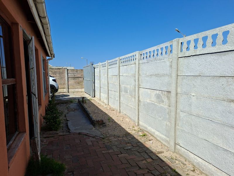 Side yard area featuring a precast concrete boundary wall, brick paving, and a metal security gate providing access to the property.