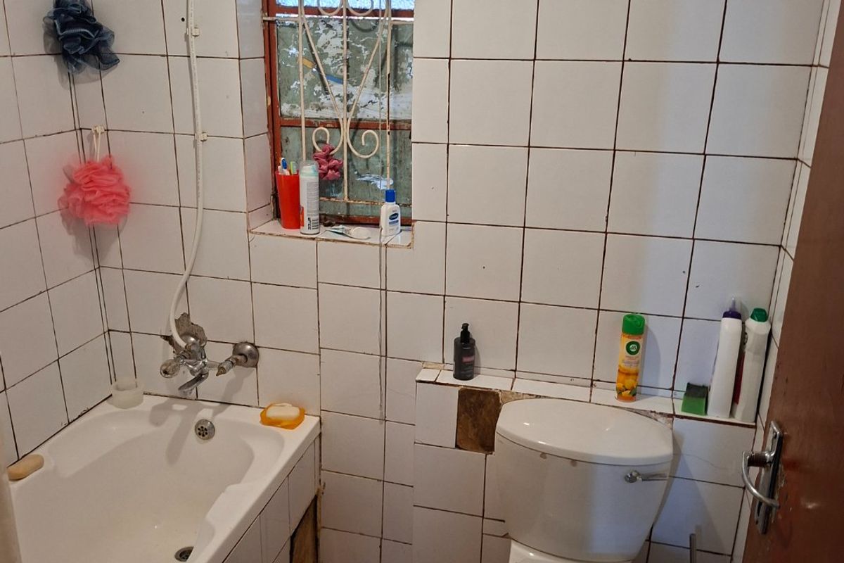 A compact bathroom featuring a bathtub, toilet, and tiled finishes, currently requiring maintenance and cosmetic updates to improve its overall condition.