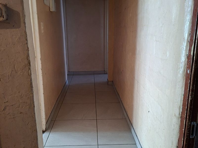 A functional hallway featuring neutral ceramic floor tiles and basic wall finishes, providing access to adjacent rooms within the property.
