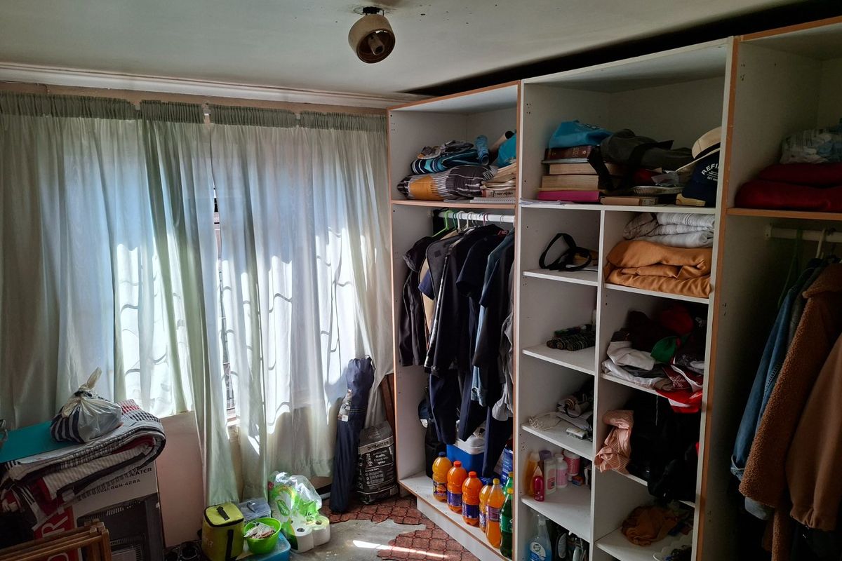 A bedroom featuring a built-in wardrobe and window with curtains. The room requires maintenance, particularly to the ceiling finish.