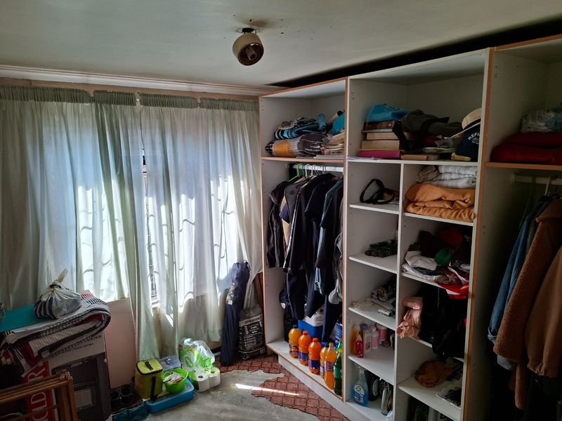A bedroom featuring a built-in wardrobe and window with curtains. The room requires maintenance, particularly to the ceiling finish.