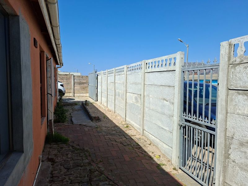 Side exterior area featuring a precast concrete boundary wall, metal security gate, and brick paved pathway along the side of the house.