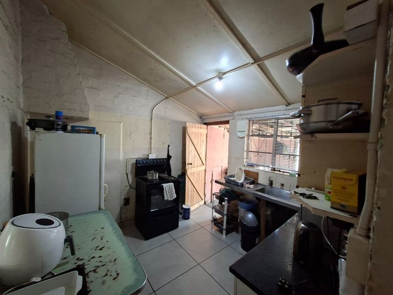 A functional kitchen space featuring tiled floors, a freestanding stove, and a stainless steel sink, requiring cosmetic updates and wall finishing.