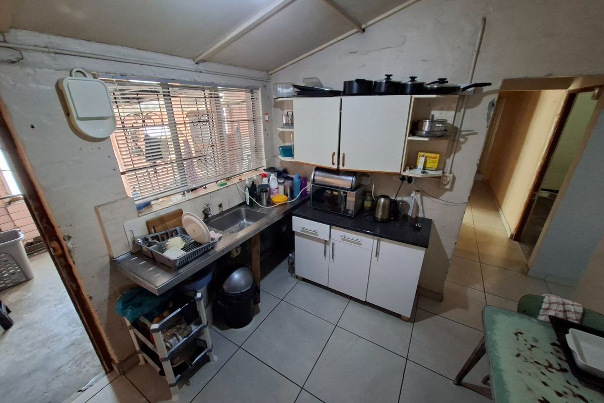 A compact kitchen featuring built-in cabinetry, a stainless steel sink, and tiled flooring, currently requiring significant cosmetic updates and maintenance.