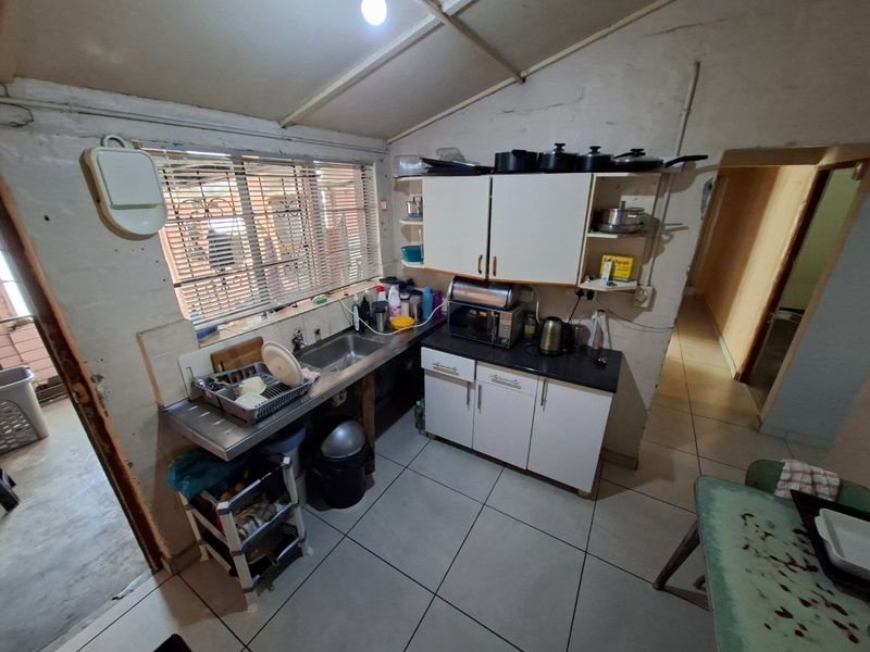 A compact kitchen featuring built-in cabinetry, a stainless steel sink, and tiled flooring, currently requiring significant cosmetic updates and maintenance.