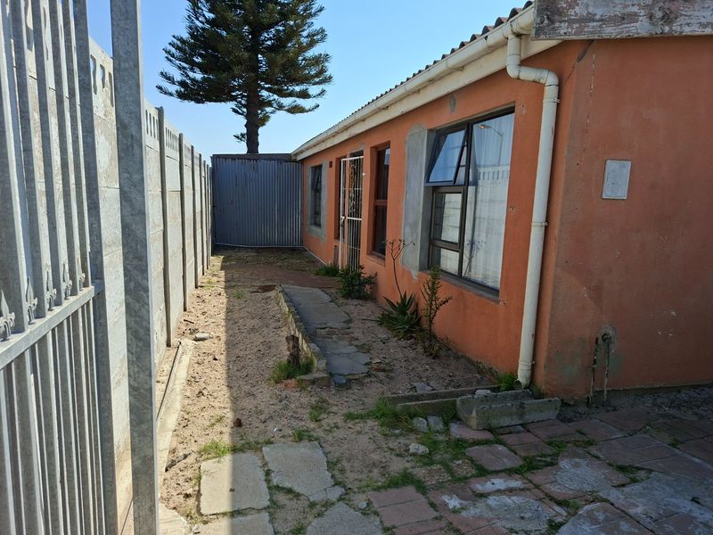 Rear exterior view of the property featuring a side walkway, precast boundary wall, and weathered exterior finishes with aluminium window frames.