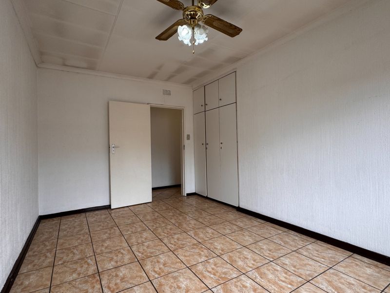 An empty bedroom featuring tiled flooring, built-in cupboards, and a ceiling fan, requiring cosmetic updates to the ceiling and finishes.