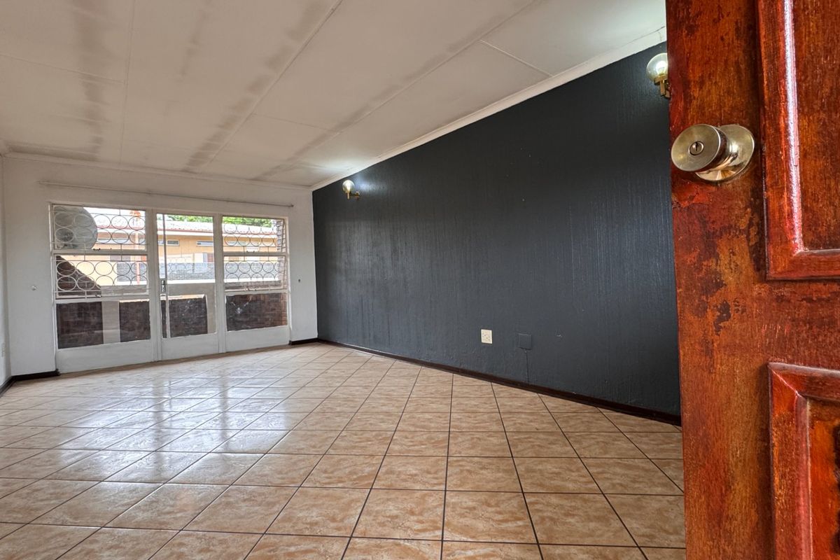 An empty living room featuring tiled flooring, a dark accent wall, and a sliding glass door with security gate leading to an outdoor area.