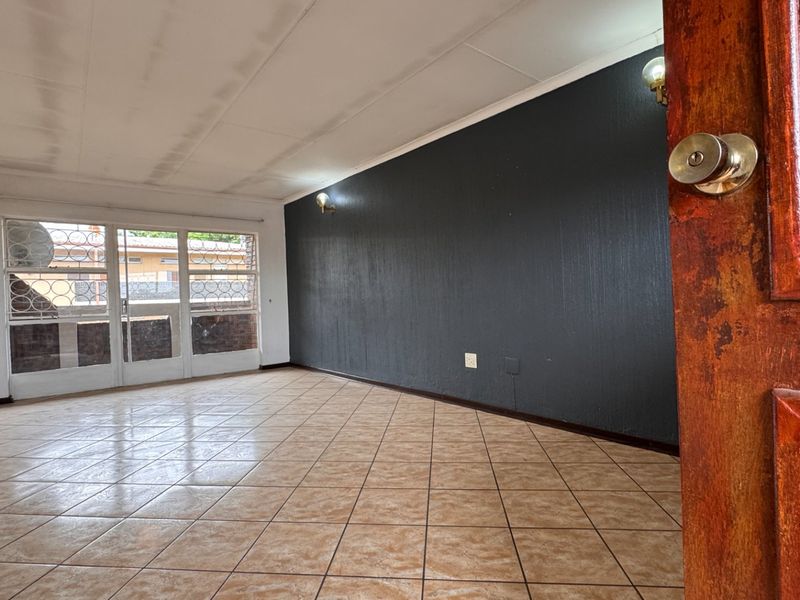 An empty living room featuring tiled flooring, a dark accent wall, and a sliding glass door with security gate leading to an outdoor area.