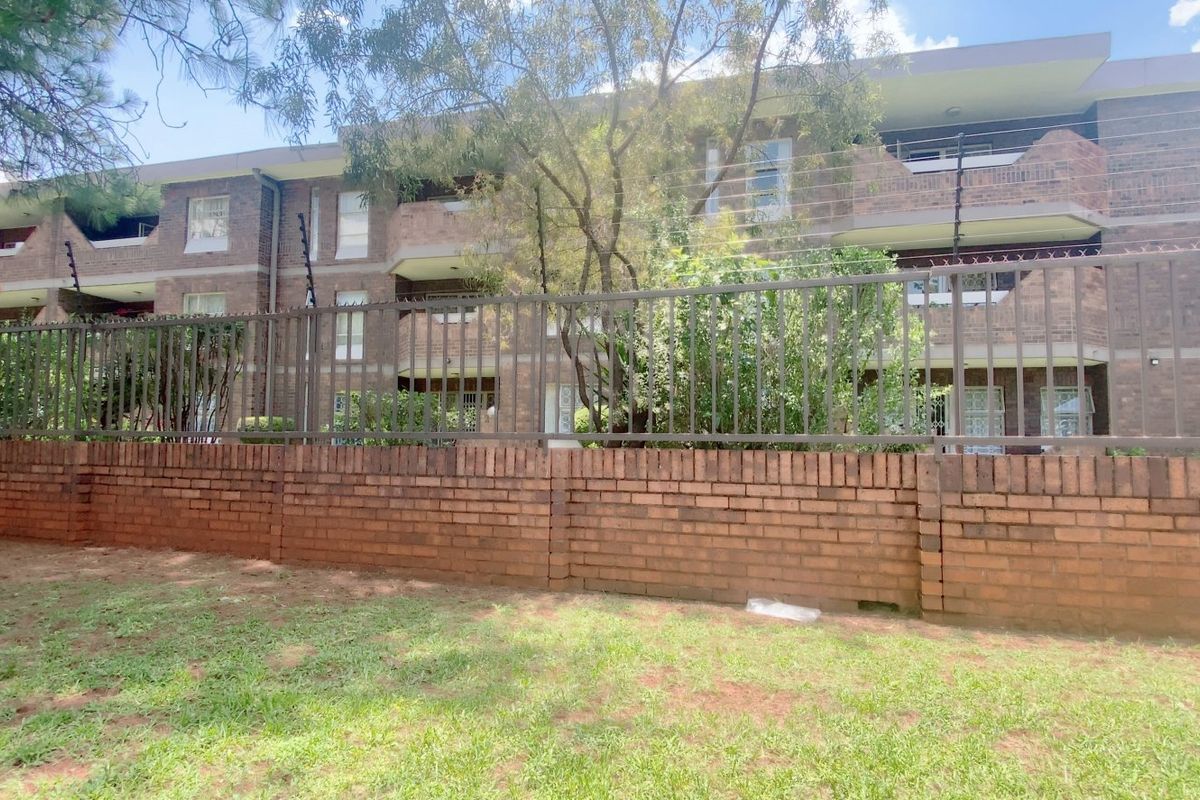 Exterior view of a multi-story face brick apartment complex featuring private balconies and secure perimeter fencing.