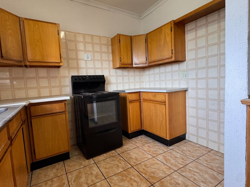 A functional kitchen featuring wooden cabinetry, laminate countertops, a double bowl sink, and a freestanding stove, finished with ceramic wall and floor tiles.