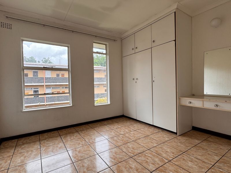 A vacant bedroom featuring built-in cupboards, a wall-mounted vanity, tiled flooring, and large windows providing natural light.