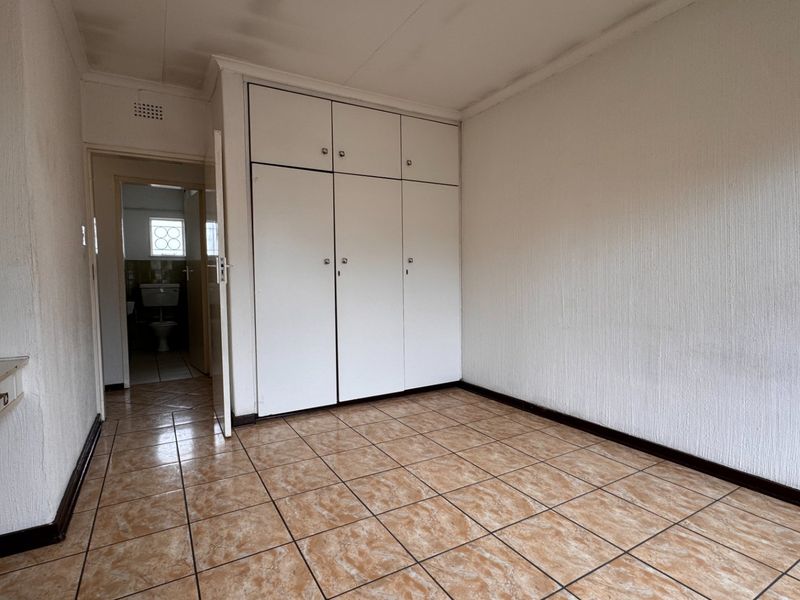 An empty bedroom featuring built-in cupboards, tiled flooring, and direct access to an adjacent bathroom.