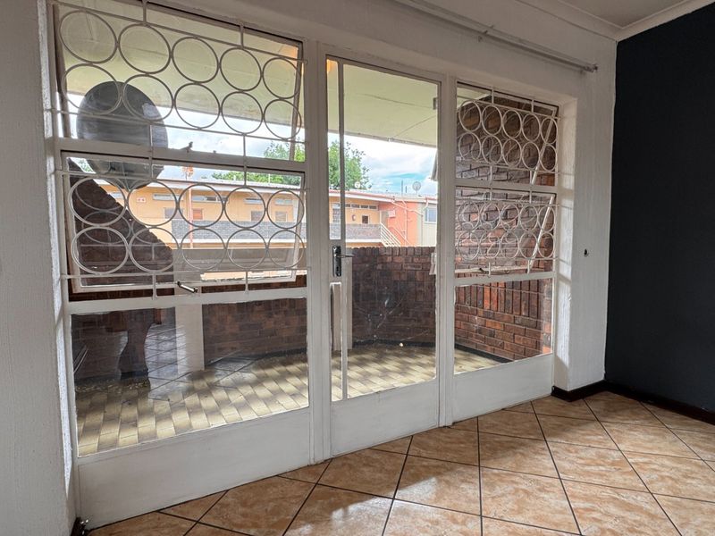 An empty living area featuring tiled flooring and large glass doors leading to a private balcony with brick wall detailing.