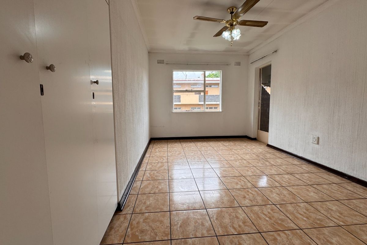 An empty bedroom featuring tiled flooring, built-in cupboards, and a ceiling fan, offering a blank canvas for renovation or interior design.