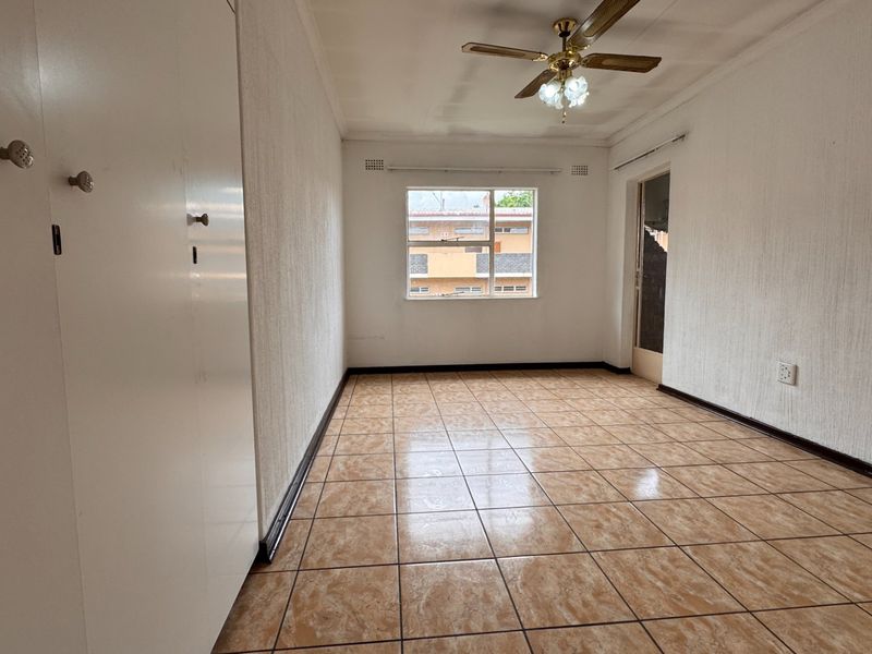 An empty bedroom featuring tiled flooring, built-in cupboards, and a ceiling fan, offering a blank canvas for renovation or interior design.