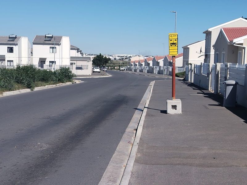 A view of a residential street featuring paved roads, sidewalks, boundary walls, and a public bus stop sign.