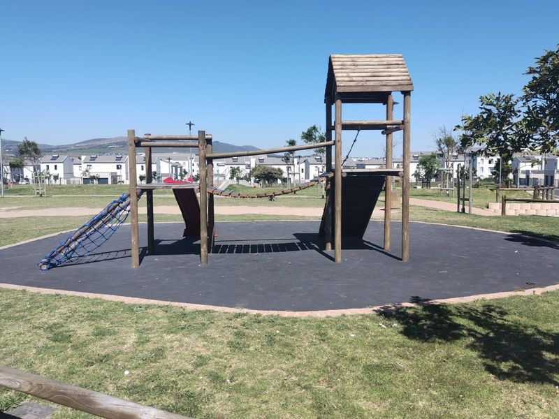 A well-maintained outdoor playground area featuring wooden climbing structures and rubberized safety surfacing within a residential estate setting.