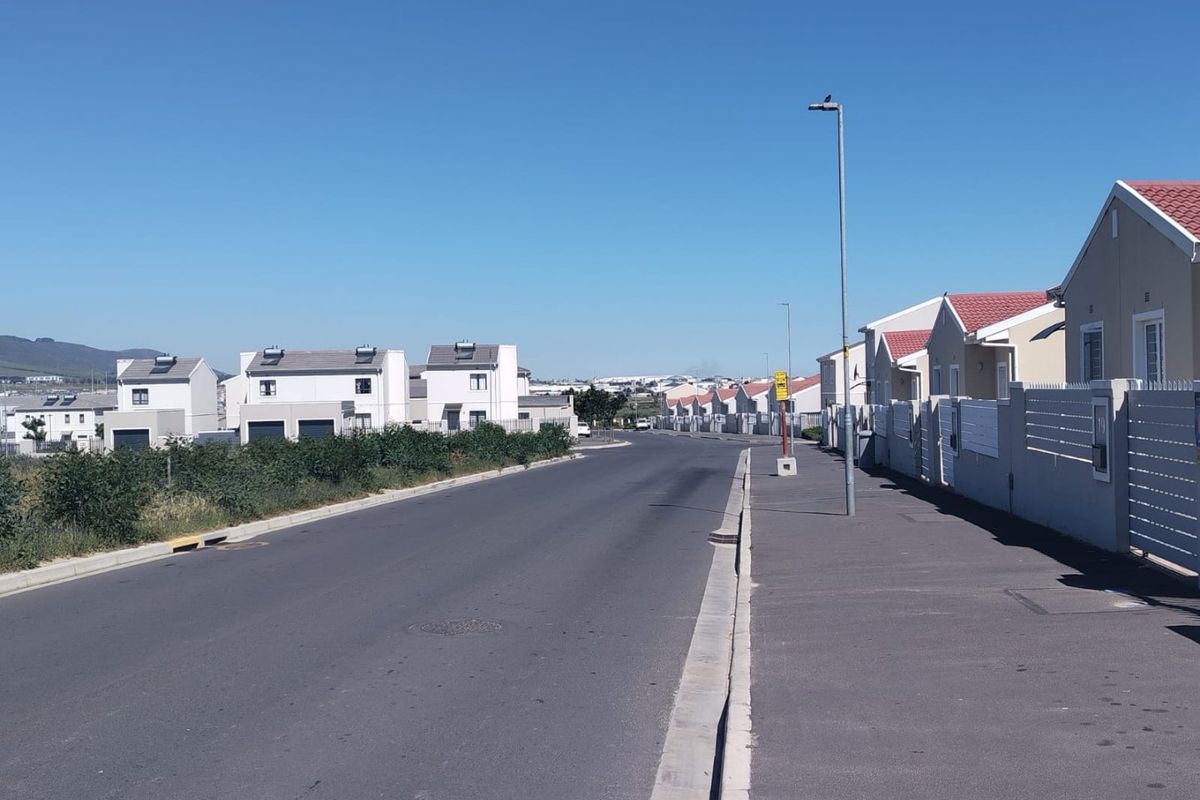 A clear street view of a modern residential estate featuring paved roads, sidewalks, and uniform housing units with solar water heating systems.