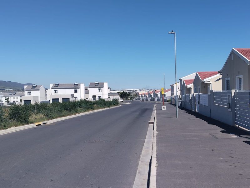 A clear street view of a modern residential estate featuring paved roads, sidewalks, and uniform housing units with solar water heating systems.