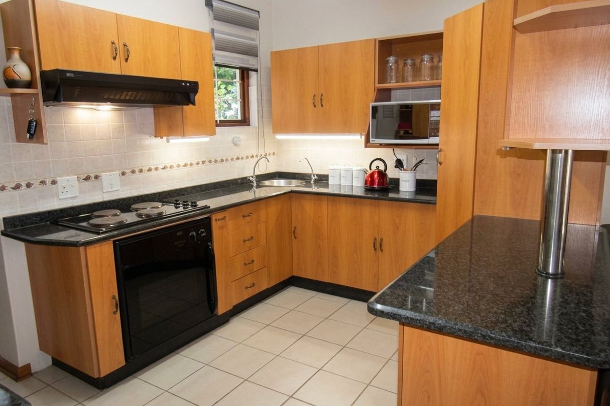 A functional kitchen featuring wood-look laminate cabinetry, dark granite countertops, built-in appliances, and tiled flooring with a neutral backsplash.