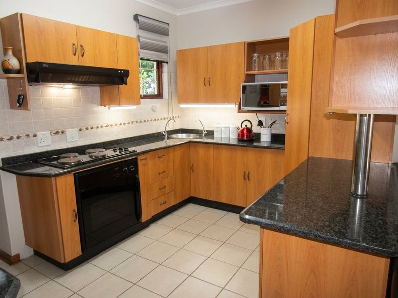 A functional kitchen featuring wood-look laminate cabinetry, dark granite countertops, built-in appliances, and tiled flooring with a neutral backsplash.
