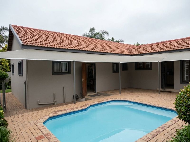 Rear exterior view featuring a swimming pool with brick paving, a covered patio area with a shade sail, and a tiled roof.