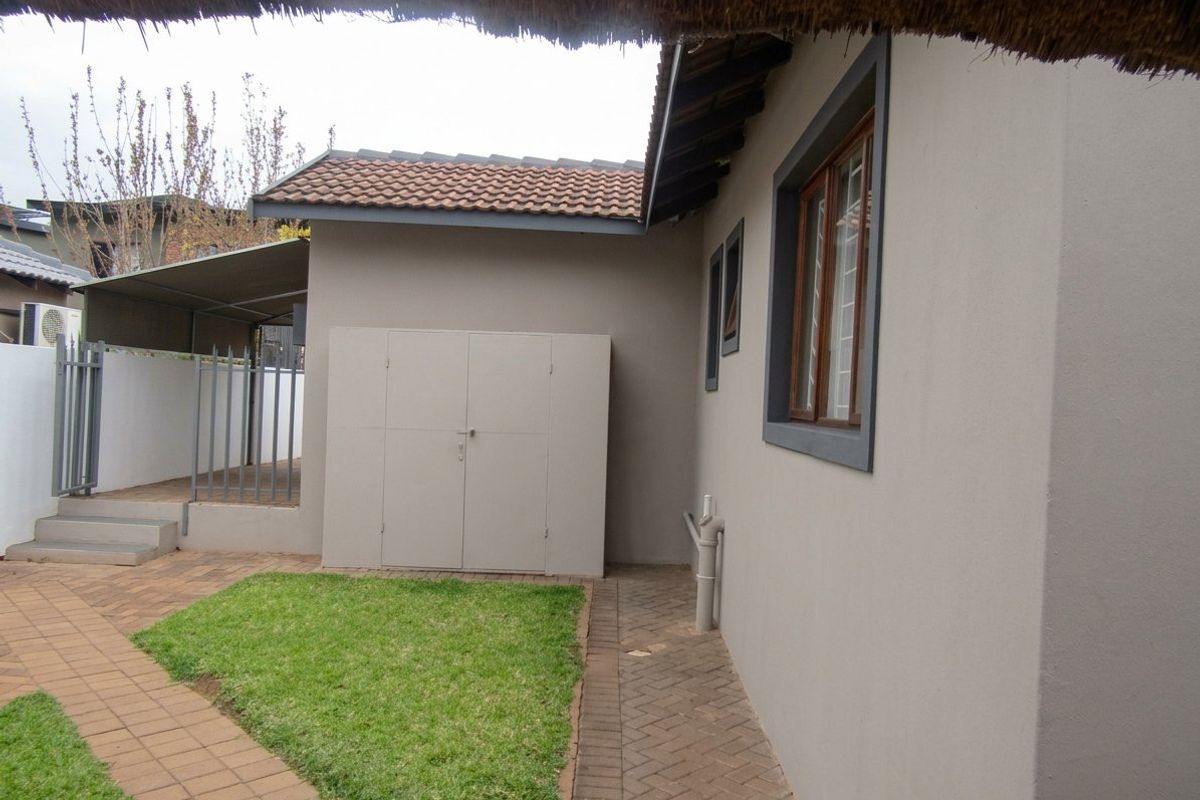 Rear exterior view showing a paved courtyard, small lawn area, built-in storage unit, and tiled roof structure.
