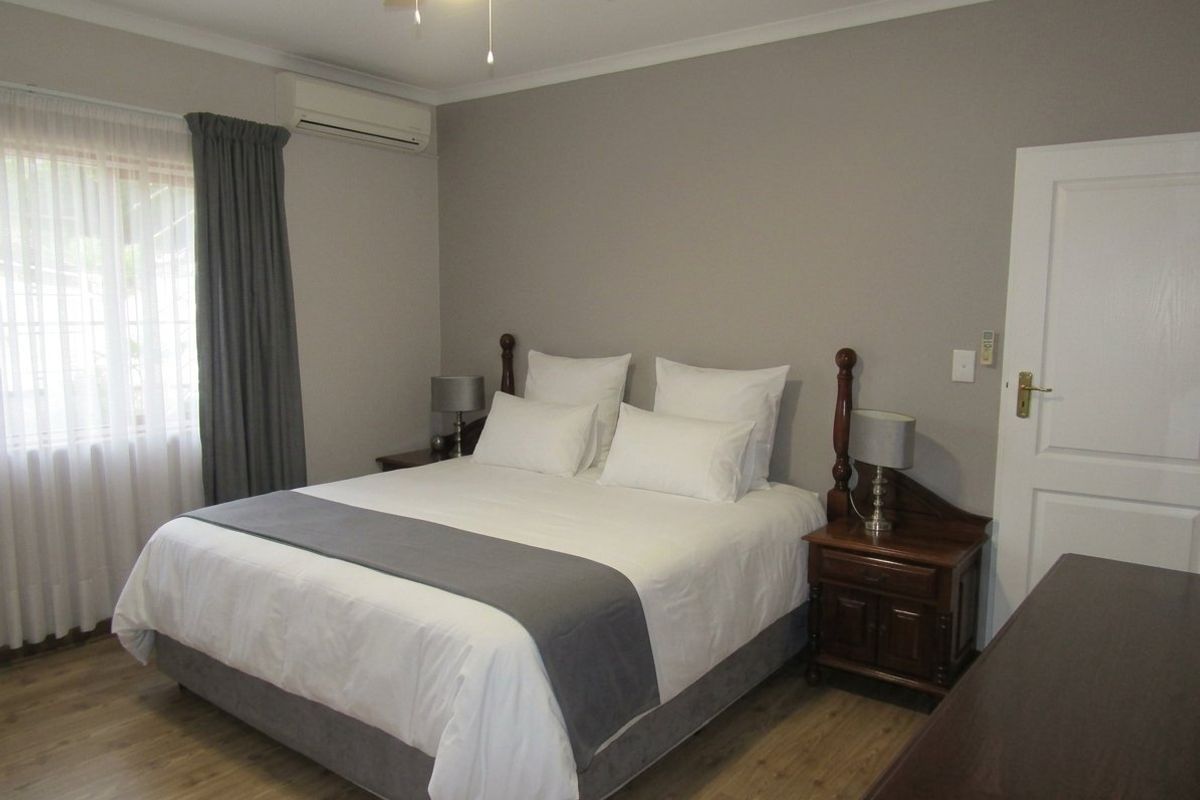 A well-maintained bedroom featuring laminate flooring, a ceiling fan, and a wall-mounted split-system air conditioner.
