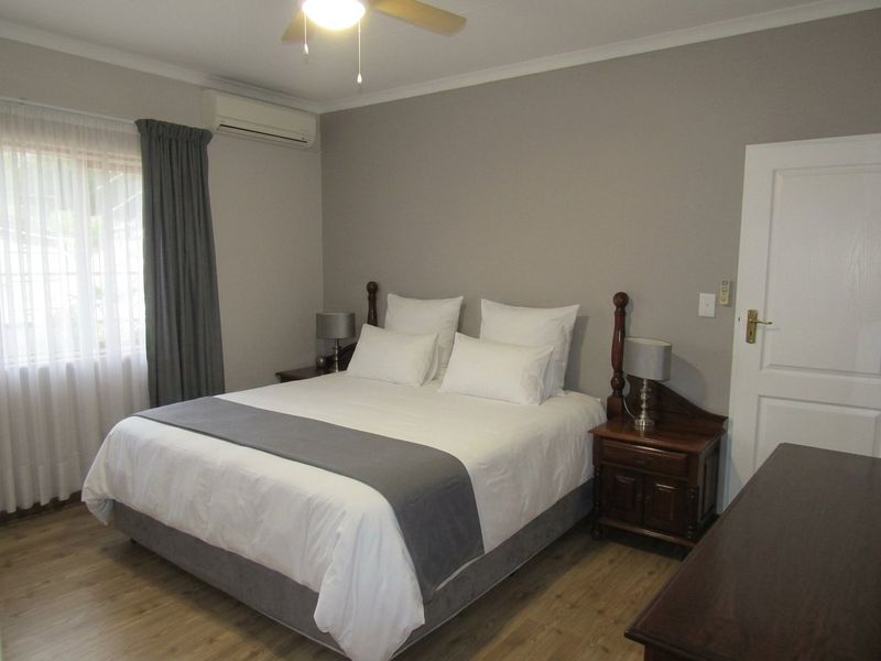 A well-maintained bedroom featuring laminate flooring, a ceiling fan, and a wall-mounted split-system air conditioner.