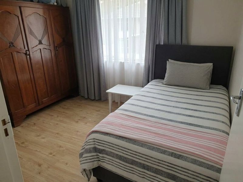 A functional bedroom featuring light-toned laminate flooring and large windows with installed curtain tracks.