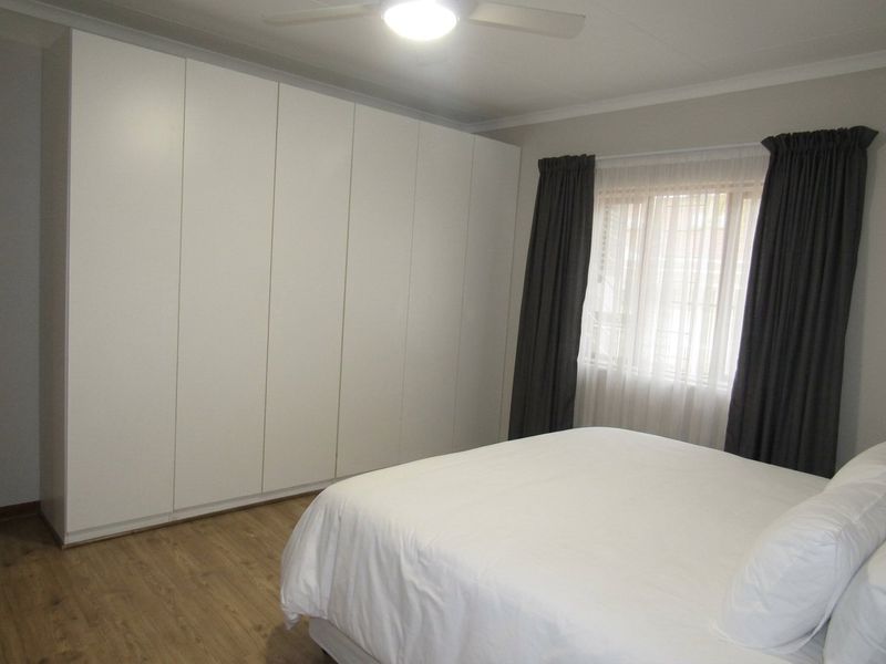 A well-maintained bedroom featuring extensive floor-to-ceiling built-in cupboards, laminate flooring, and a ceiling fan for climate control.