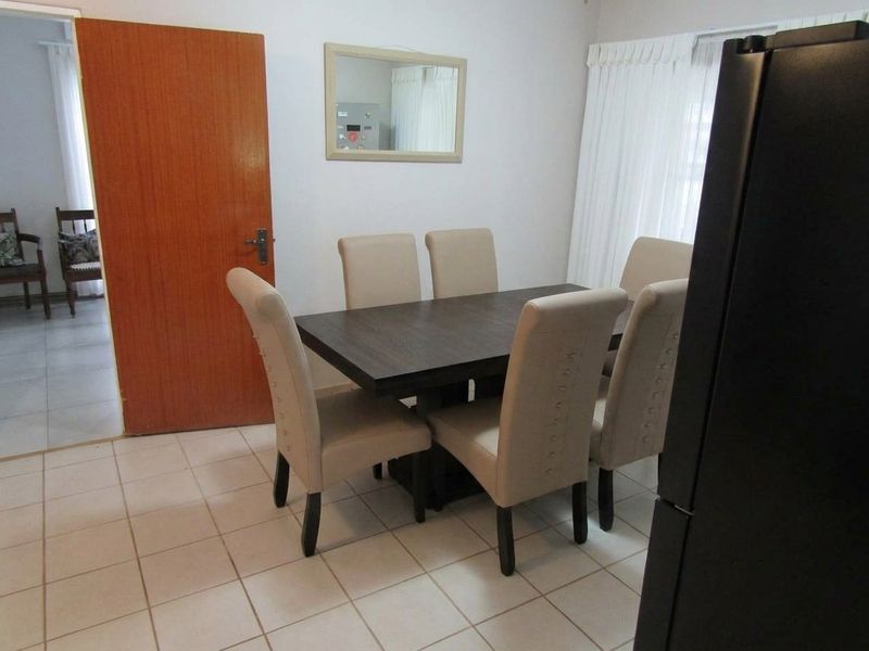 A functional dining area featuring neutral tiled flooring and a solid timber door, providing a clean and simple space for family meals.