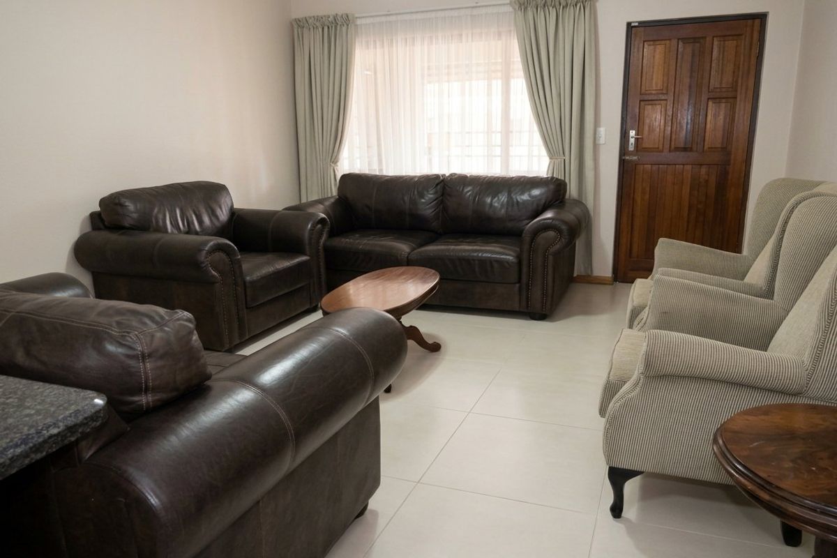 A spacious living room featuring neutral tiled flooring and a solid wooden door, providing a comfortable and functional area for relaxation.