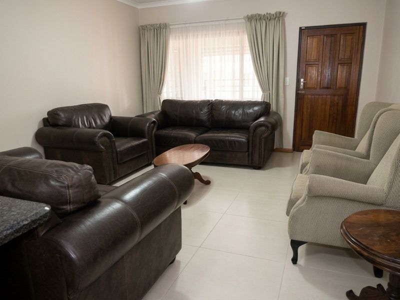 A spacious living room featuring neutral tiled flooring and a solid wooden door, providing a comfortable and functional area for relaxation.