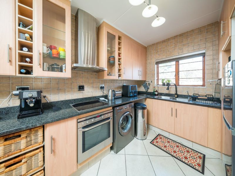 A functional kitchen featuring light wood cabinetry, granite countertops, a stainless steel extractor fan, built-in oven, and tiled finishes throughout.