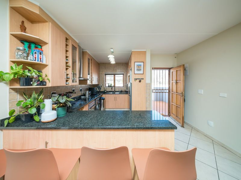 A functional kitchen featuring light wood cabinetry, dark granite countertops, and tiled flooring, with direct access to an outdoor area via a security door.