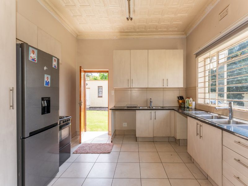 A functional kitchen featuring built-in cabinetry, double sink, tiled flooring, and direct access to the rear garden area.