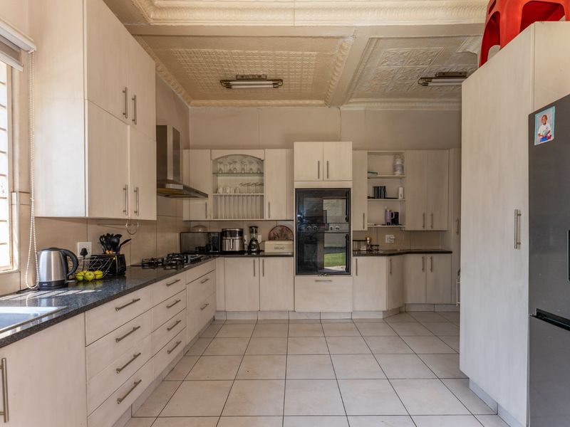 A functional kitchen featuring light-toned built-in cabinetry, granite countertops, a gas hob, and a distinctive pressed metal ceiling.