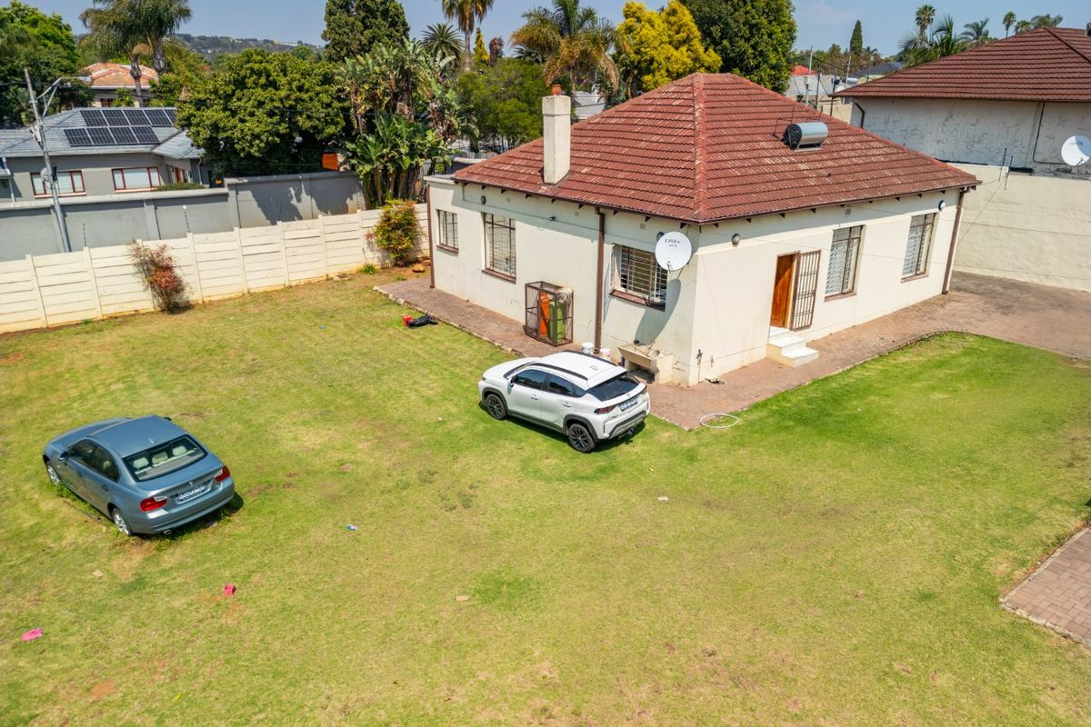 Aerial view of the rear elevation of a detached house featuring a tiled roof, solar water heater, and a spacious grass garden.