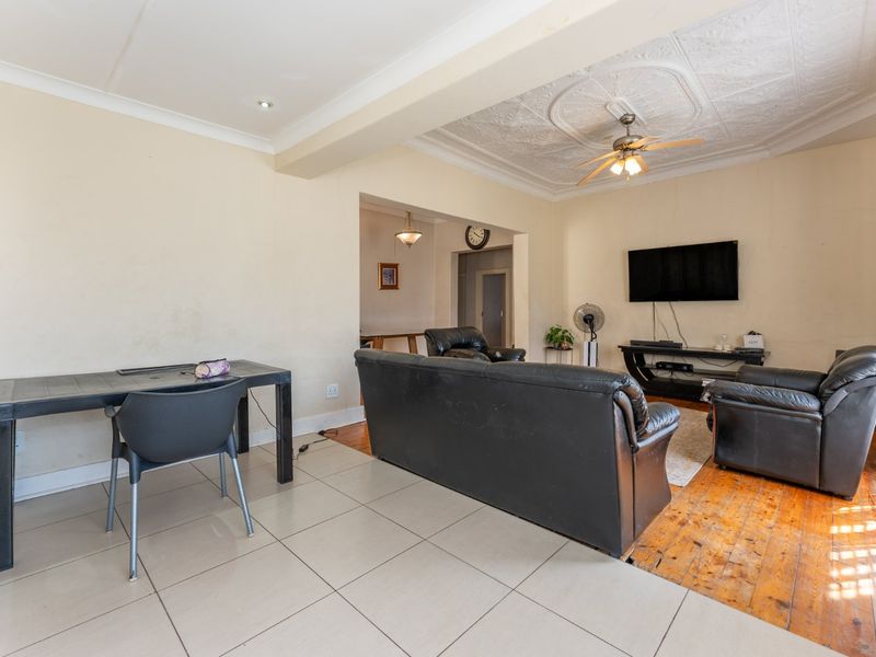 Open plan living area featuring a mix of tiled and hardwood flooring, decorative ceiling detailing, and a ceiling fan.