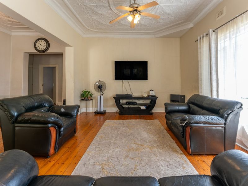 Spacious living room featuring original hardwood flooring and an ornate pressed metal ceiling, offering a classic architectural foundation for modern updates.