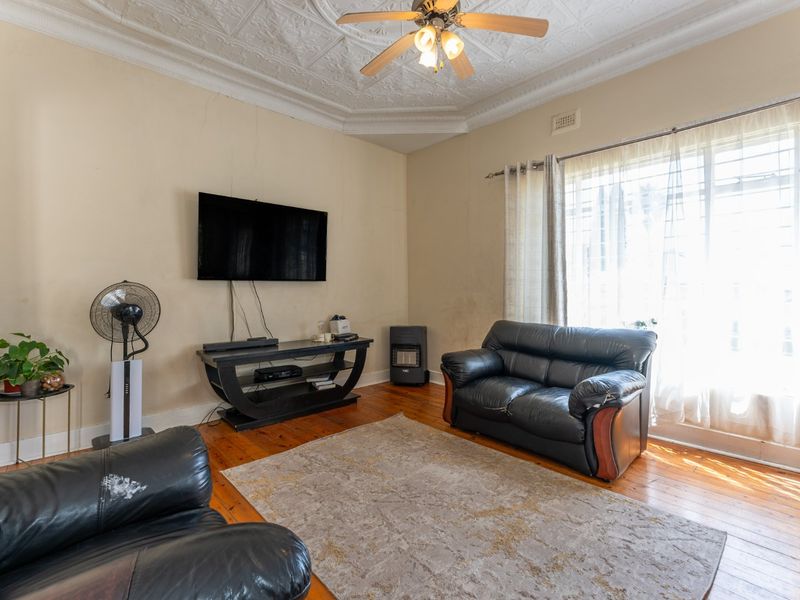 Living room featuring original decorative pressed metal ceilings, timber flooring, and a built-in gas heater, requiring cosmetic updates to the walls.
