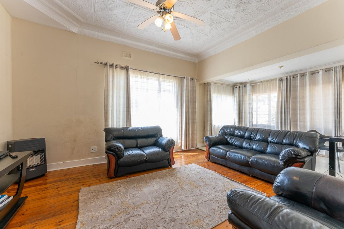 Spacious living room featuring original decorative plaster ceilings, polished hardwood flooring, and a built-in gas heater, offering a classic character aesthetic.
