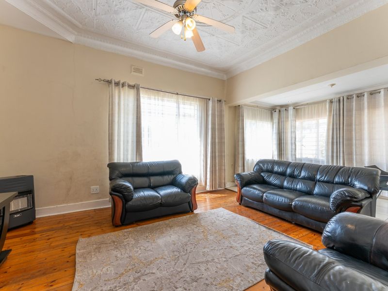 Spacious living room featuring original decorative plaster ceilings, polished hardwood flooring, and a built-in gas heater, offering a classic character aesthetic.
