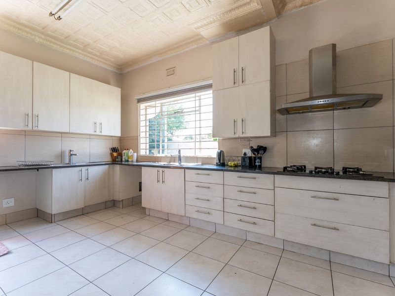 A functional kitchen featuring light-toned built-in cabinetry, a gas hob with extractor fan, tiled backsplash, and a distinctive pressed metal ceiling.