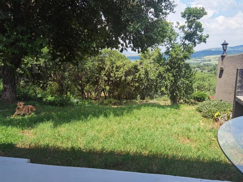 A scenic view of the lush green farm landscape and surrounding hills, featuring mature trees and a well-maintained garden area.