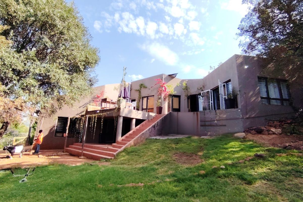 Rear view of the farm property featuring a raised patio, concrete staircase, and large windows overlooking the garden area.